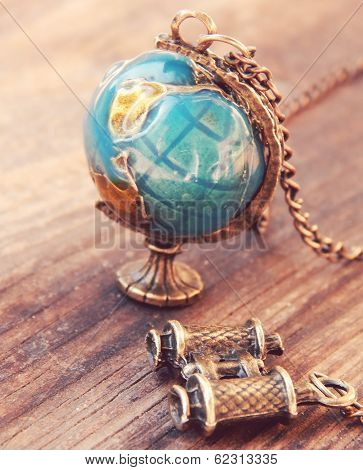 Necklace in the form of Earth globe and binoculars on a wooden background