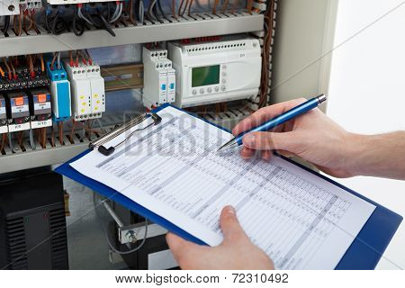 Electrician Holding Clipboard While Examining Fusebox
