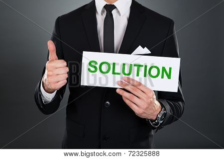 Businessman Gesturing Thumbsup While Holding Solution Sign