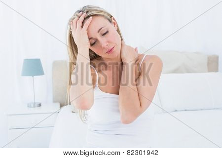 Upset blonde suffering from headache and neck pain at home in the bedroom