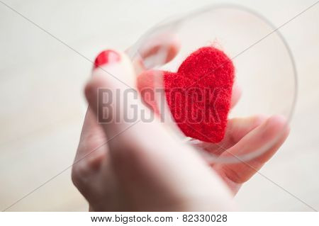 Woman's hand is holding glass with felt heart