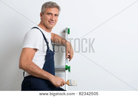 Happy Mature Painter Standing On Stepladder Holding Brush