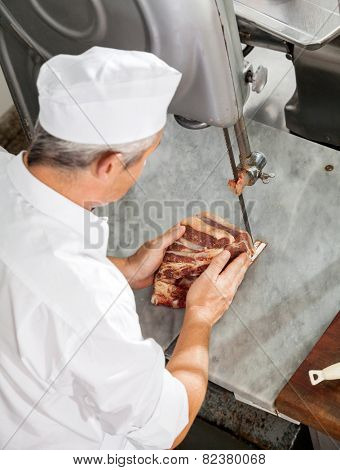 High angle view of butcher cutting fresh meat with bandsaw in butchery