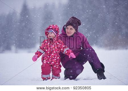 happy family on winter vacation, mom and cute little girl have fun and slide while snow falkes falling