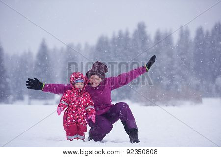 happy family on winter vacation, mom and cute little girl have fun and slide while snow falkes falling