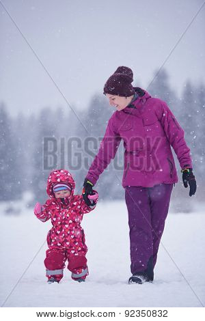 happy family on winter vacation, mom and cute little girl have fun and slide while snow falkes falling