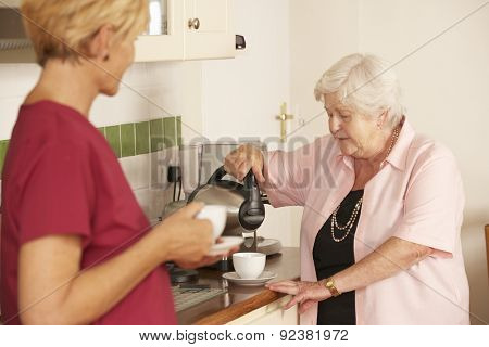 Home Help Sharing Cup Of Tea With Senior Woman In Kitchen