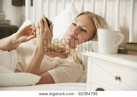 Woman In Bed At Home Texting On Mobile Phone