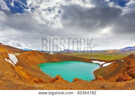 Summer in Iceland. Picturesque lake in the crater of an extinct volcano. Lake water bright green color. On the shores lie snowfields from last year