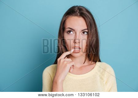 Close-up portrait of a pensive thougtful pretty girl thinking about something isolated on the blue background