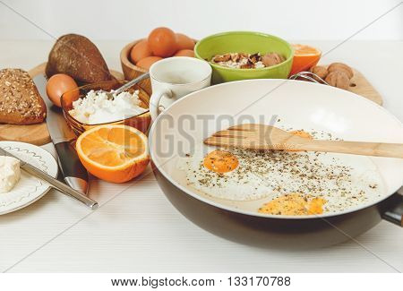 Fried Eggs in the Frying Pan,Breakfast Ingredients.Orange,Bread,Butter.Kitchen Accessories.Cooking Morning Food.White Table.Selective Focus