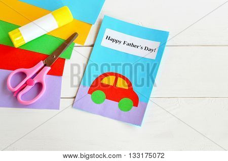Paper card with red car and text Happy father's day. Colored paper, scissors, glue stick. Materials used in manufacture of handmade card. Paper handcraft greeting card for dad. Children creative craft