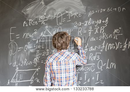 Boy with chalk writting on math formulas black board