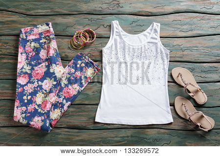 Floral trousers and tank top. Beige sandals and white top. Girl's newly purchased clothing. Set of colorful bracelets.