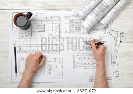 Close-up hands of man holding an engineering divider over drawing plan in top view.  Workplace of architect or constructor. Engineering work. Construction and architecture. Architect drawing. Measurement. Draftsmanship.