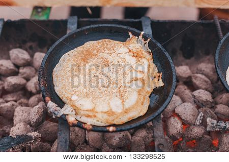 Pancakes are fried on coals in a cast iron skillet
