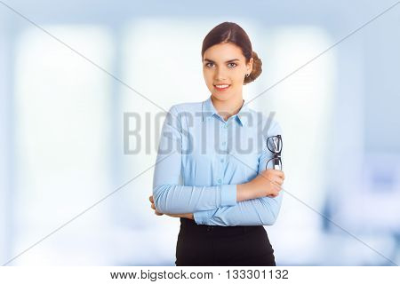 Portrait of happy smiling young cheerful businesswoman in blue clothing. With glasses in crossed arms pose.