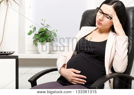 Tired pregnant woman sitting at workplace in the office