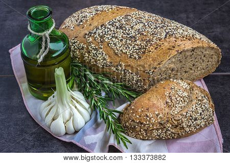 Whole wheat bread and rye sprinkled with sunflower seeds poppy seeds sesame seeds next to a bottle of olive oil rosemary and garlic