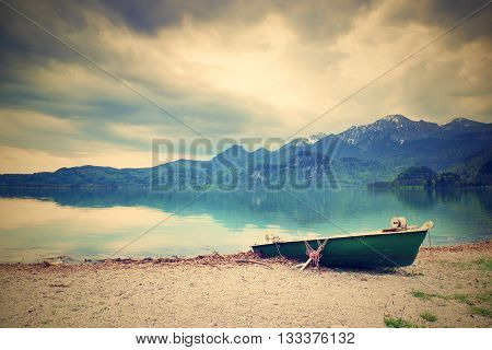 Abandoned Fishing Paddle Boat On Bank Of Alps Lake. Morning Lake Glowing By Sunlight.