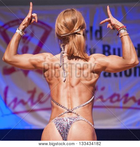 MAASTRICHT THE NETHERLANDS - OCTOBER 25 2015: Female fitness model flexes her muscles and shows her best physique in a back doiuble biceps pose on stage at the World Grandprix Bodybuilding and Fitness of the WBBF-WFF