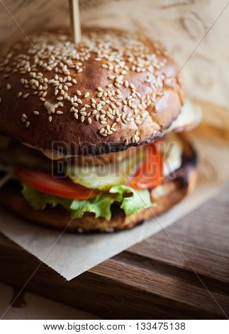 Delicious burger with lamb steak tomato cucumber and fresh salad fried on a grill and put between two bagels with sesame seeds. Unhealthy but so tasty junk food. Close up photo in macro mode no models
