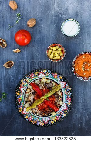 Traditional Turkish Bursa iskender kebap doner served with special red sauce and yogurt in the middle, garnished with grilled tomatoes and peppers