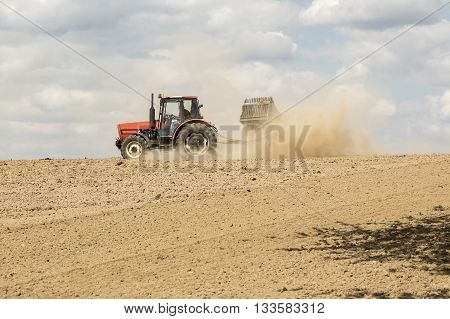 Tractor ploughing a field with a trail of dust behind it. Blue sky above.