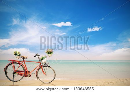 Old red Bicycle with basket flowers on beautiful beach tropical sea backgroundstyle vintage tone