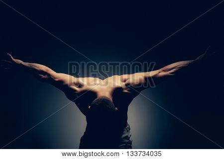 Sexy muscular male back of athlete bodybuilder posing in power with raised hands and bare torso on dark background
