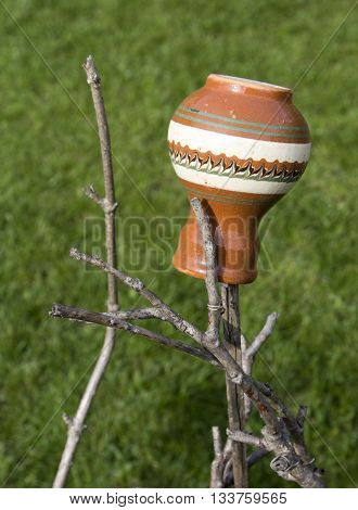 Ceramic jug hung on a stick against grassy background