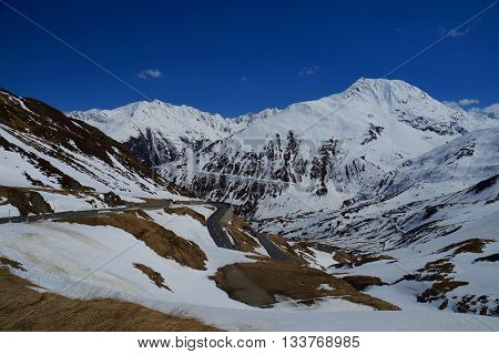 Melting snow reveals patches of dry grass and stone in late spring. Serpentine mountain road descending after passing the top of Oberalppass at 2200 m above sea level in the direction of Chur, May 2016.