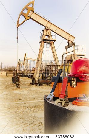 Tool box helmet and wrenches on the background of blurry pump jack. Oil and gas concept. Toned.