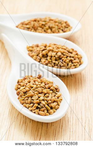 Fenugreek seeds in white spoon on wood background.