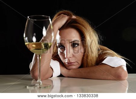 drunk blond woman alone in wasted depressed expression looking thoughtful to white wine glass isolated on black background in alcohol abuse and alcoholic housewife concept