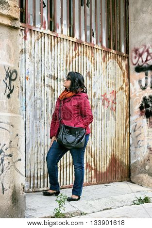 adult woman with crossbag looking up against of abandoned grunge building.