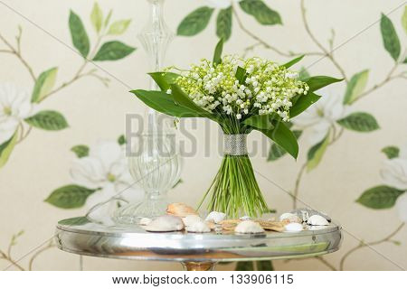 Small bouquet of Lily of the valley flowers standing on decorative fabric with floral background in the back. Flower decor idea. Flower design.