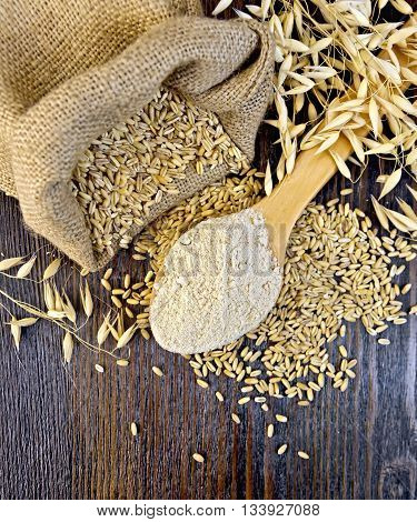 Oat flour in a wooden spoon, a bag of oats and oat stalks on a dark wooden board on top
