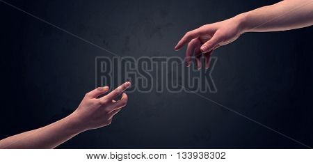 Two male hands reaching out to one another, almost touching, in front of dark clear empty background wall concept