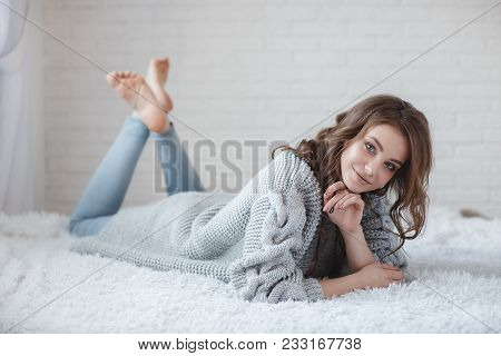 Winter Concept. Cute Young Girl In A Gray Knitted Sweater. Beautiful Woman Is Relaxing In A White Be