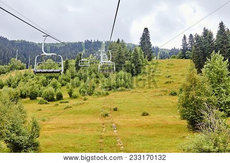 Emtpy Chairlift In Ski Resort. Mountains And Hills With In Summer With Green Trees And Grass