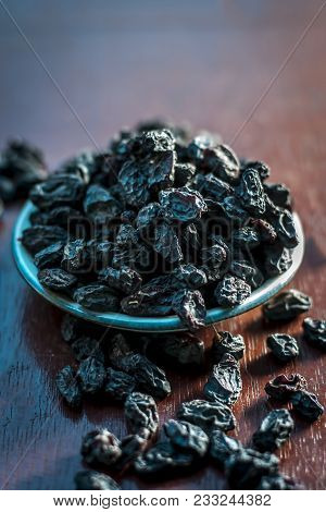Black Raisin Or Kali Kishmish Or Zante Currant In A White Plate On Wooden Surface In Dark Gothic Col