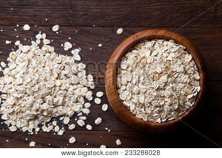 Oat Flakes In Bowl And Wooden Spoon Isolated On Dark Wooden Background, Close-up, Selective Focus, S