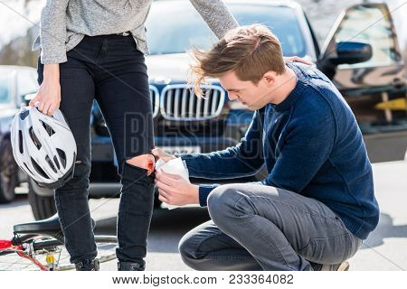 Young male driver using a sterile adhesive bandage from his first aid kit to help an injured female bicyclist on the street