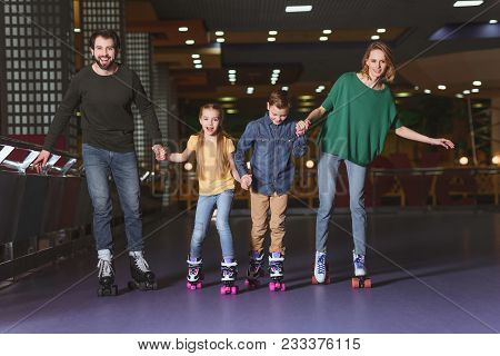 Happy Family Holding Hands While Skating Together On Roller Rink