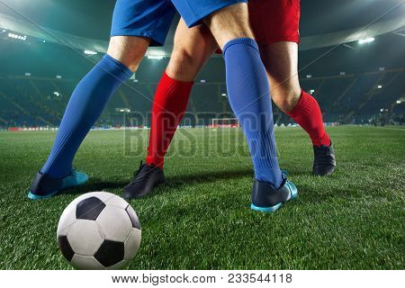 Football Players Tackling For The Ball Over Green Grass At Stadium. Professional Football Soccer Pla