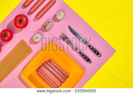 Sausages On A Orange Plate With Tomatoes, Spaghetti And Garlic On A Yellow And Pink Minimal Backgrou