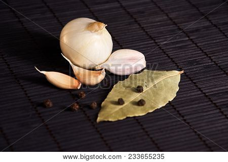 Onion, Garlic, Black Pepper And Bay Leaf On A Black Table