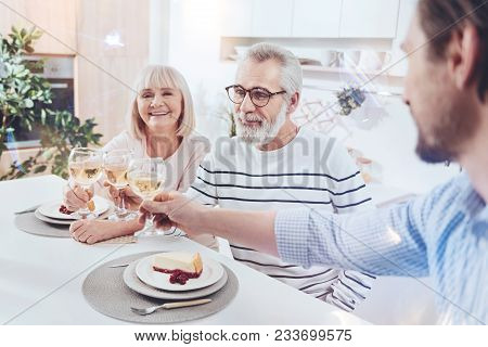 Sweet Home. Cheerful Delighetd Aged Couple Sitting At The Table And Meeting With Their Adult Son Whi