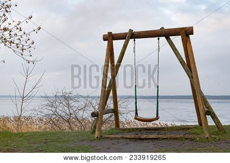 Old Wooden Swing On The Grass With View Of The Water And Sky. Off Into The Wild Blue Yonder. Alone. 